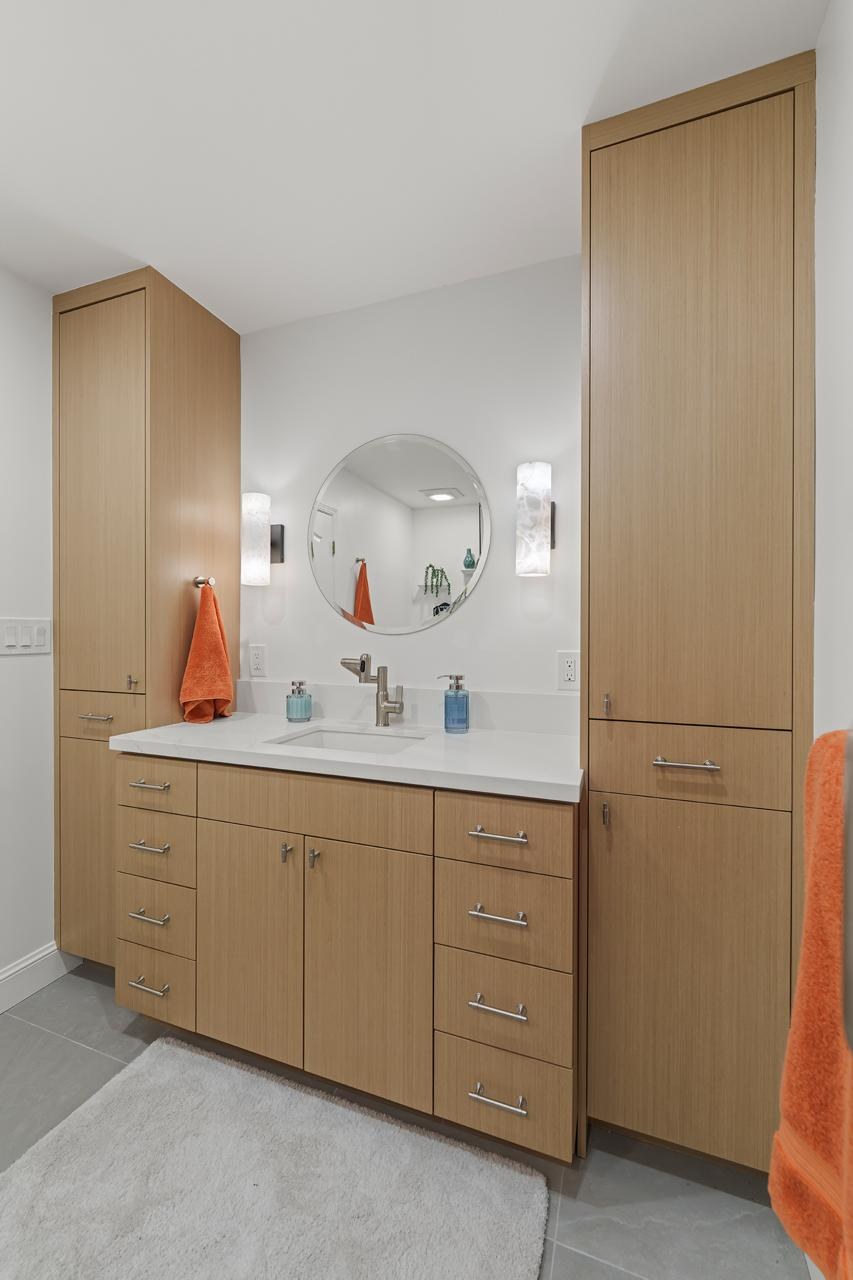 Bathroom after: floor to ceiling wood tone vanity with linen towers with light oak laminate cabinetry and white quartz countertop, by ASL Remodeling.