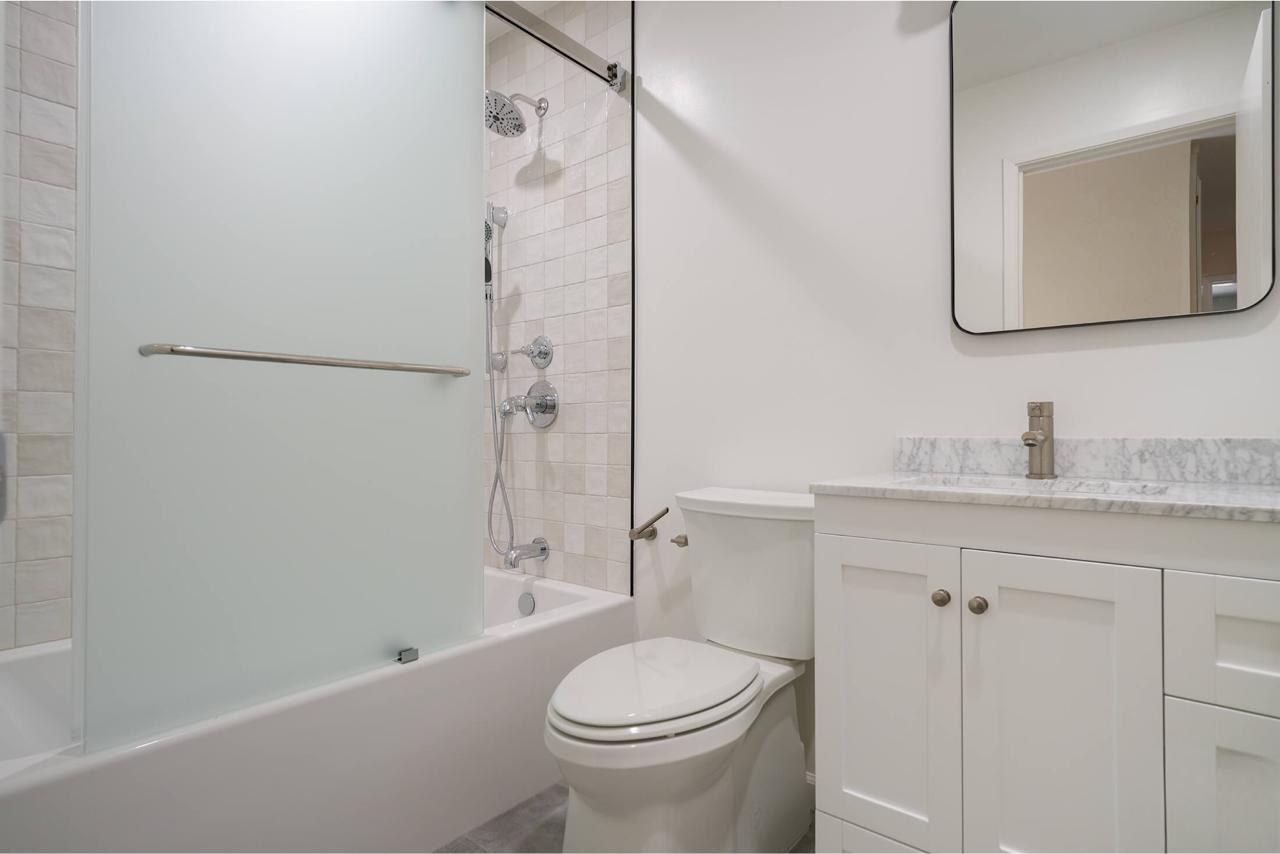 Bathroom after: frameless glass tub shower enclosure with marble countertop and ceramic subway tile, by ASL Remodeling.