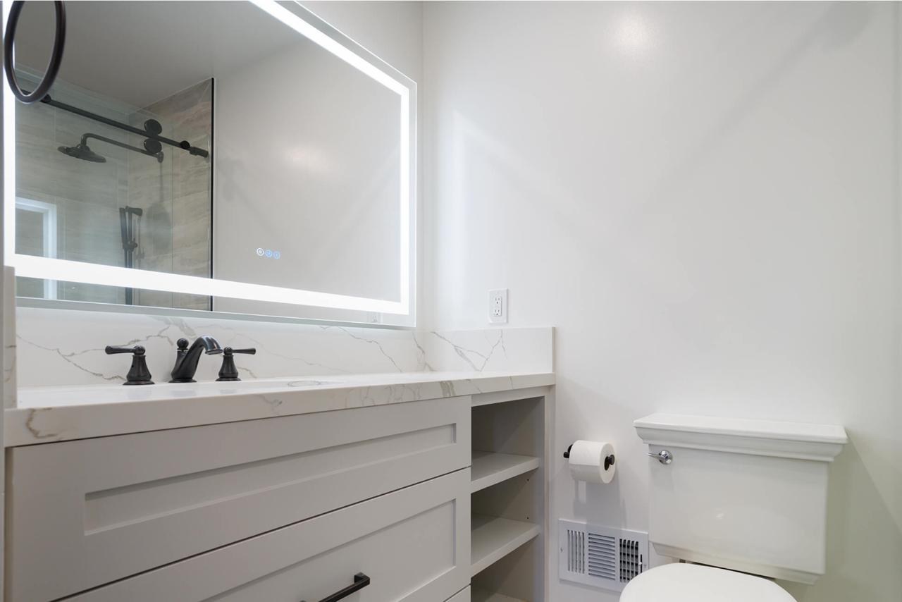 Bathroom after: LED backlit mirror over marble vanity with white quartz marble countertop and white shaker cabinetry, by ASL Remodeling.