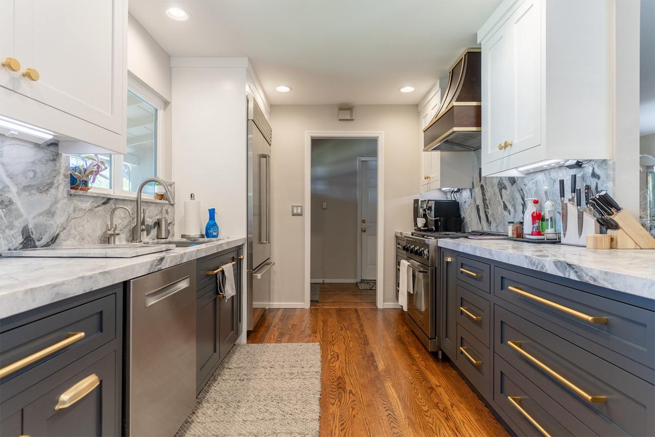 Kitchen featuring two-tone custom inset cabinetry, bookmatched marble countertops, soft brass hardware, and panel-ready appliances