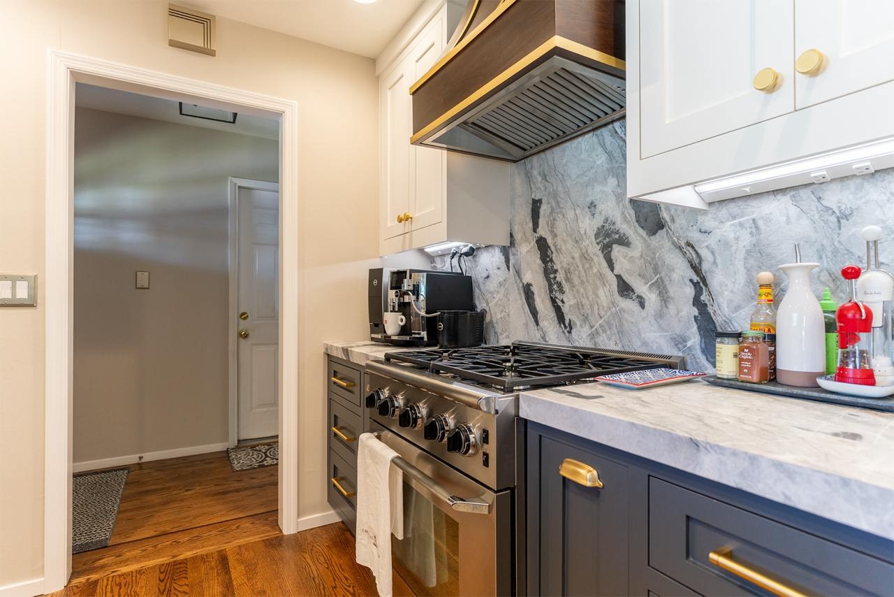 Kitchen with bookmatched marble countertops, full-height backsplash slabs, custom inset cabinetry, and soft brass hardware