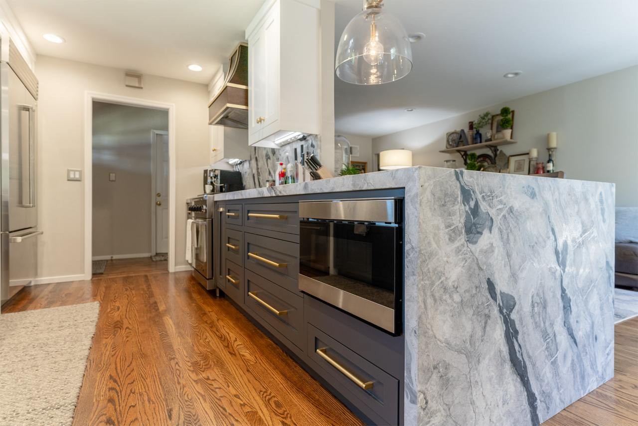 Kitchen with mini waterfall island edge, built-in microwave drawer, bookmatched marble countertops, and custom inset cabinetry