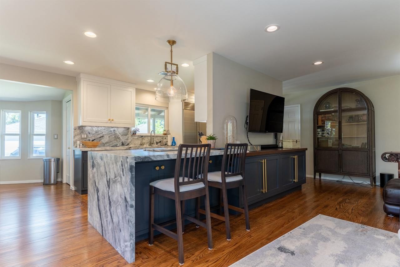 Open concept kitchen remodel with completed large center island featuring bar seating, dramatic bookmatched marble slab backsplash, pendant lighting, and arched doorway opening to dining area with hardwood floors