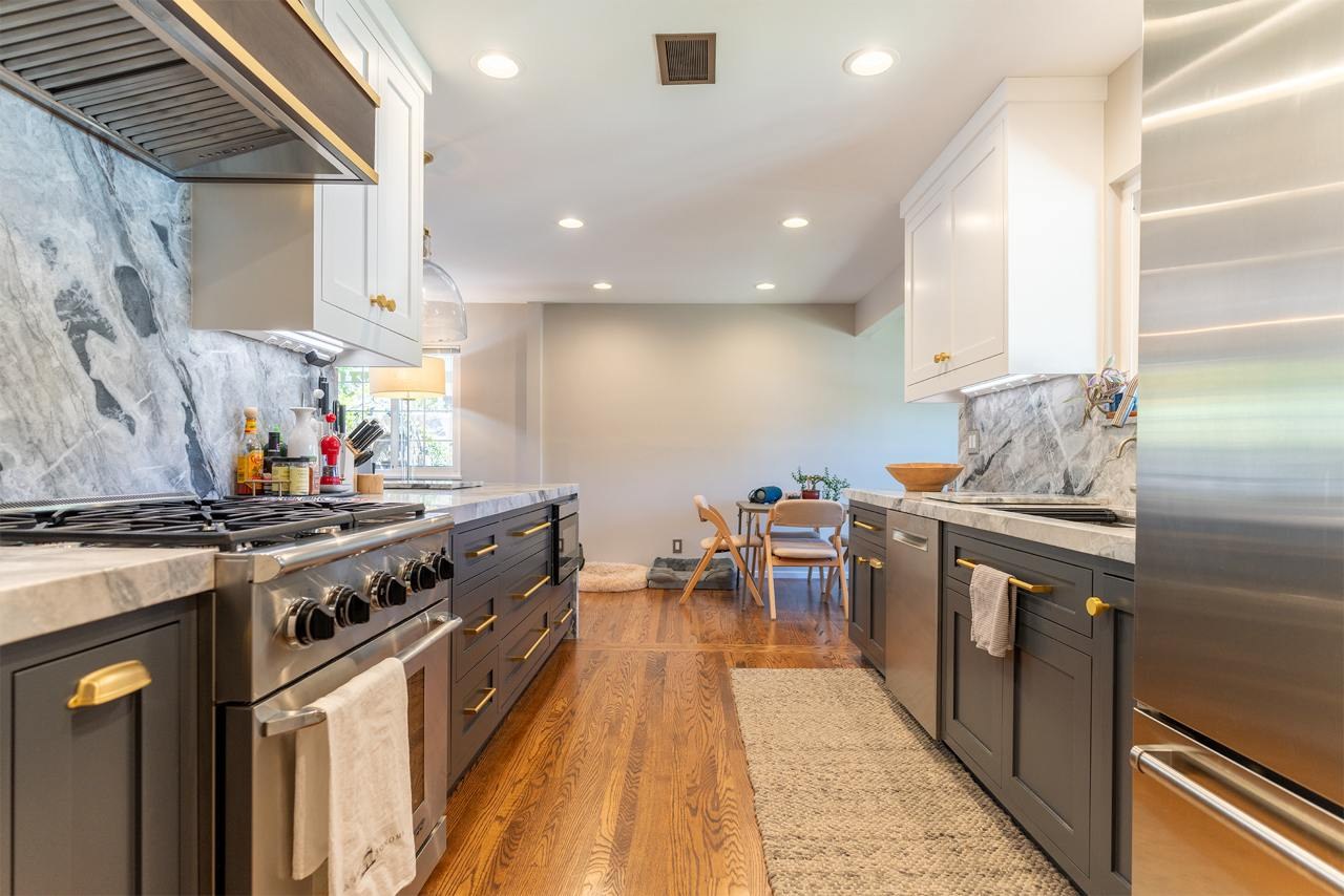 Kitchen remodeling showcasing completed two-tone custom cabinetry with white shaker uppers and dark blue lowers, hardwood plank flooring, and professional-grade stainless steel appliances