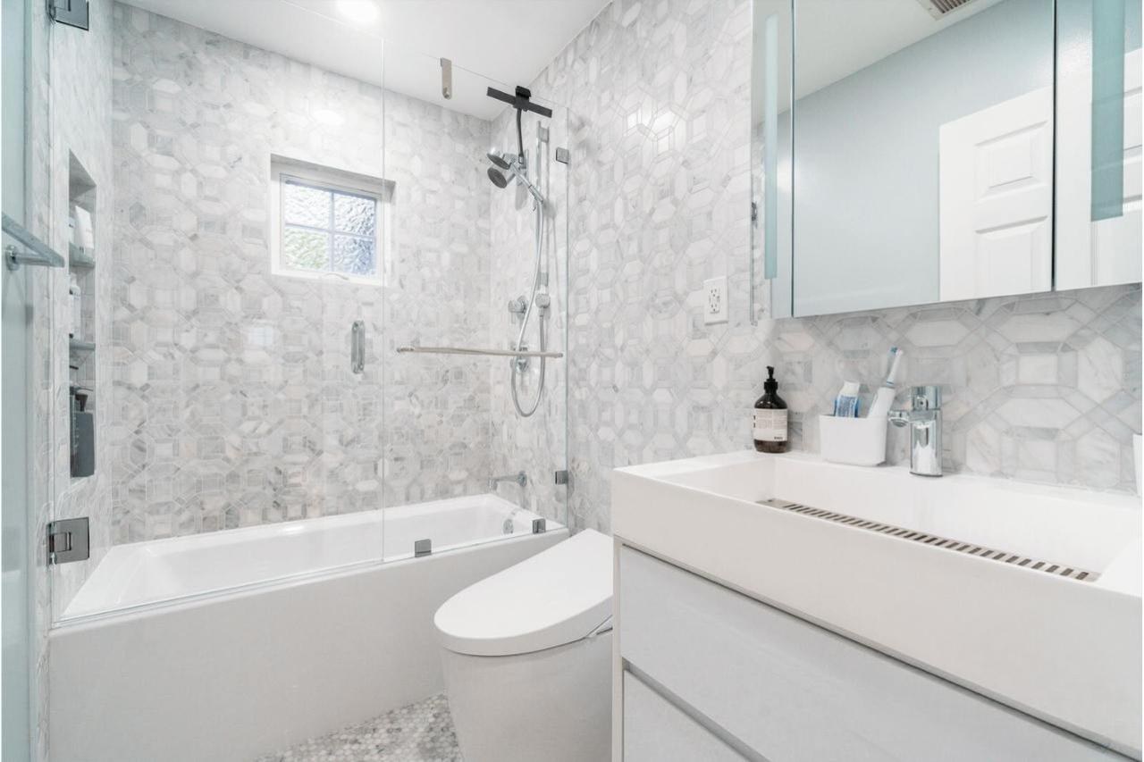 Home addition project featuring completed bathroom with natural marble wall tile, modern freestanding bathtub, white floating vanity, frameless glass shower, and modern pendant lighting