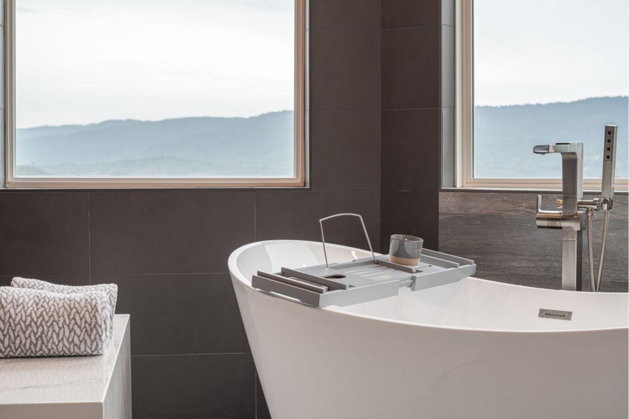 Primary bathroom: freestanding soaking tub with with white acrylic freestanding tub and large format dark porcelain tile, by ASL Remodeling.