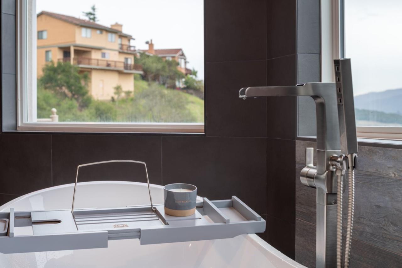 Primary bathroom: soaking tub with scenic window view with white acrylic soaking tub and dark porcelain wall tile, by ASL Remodeling.