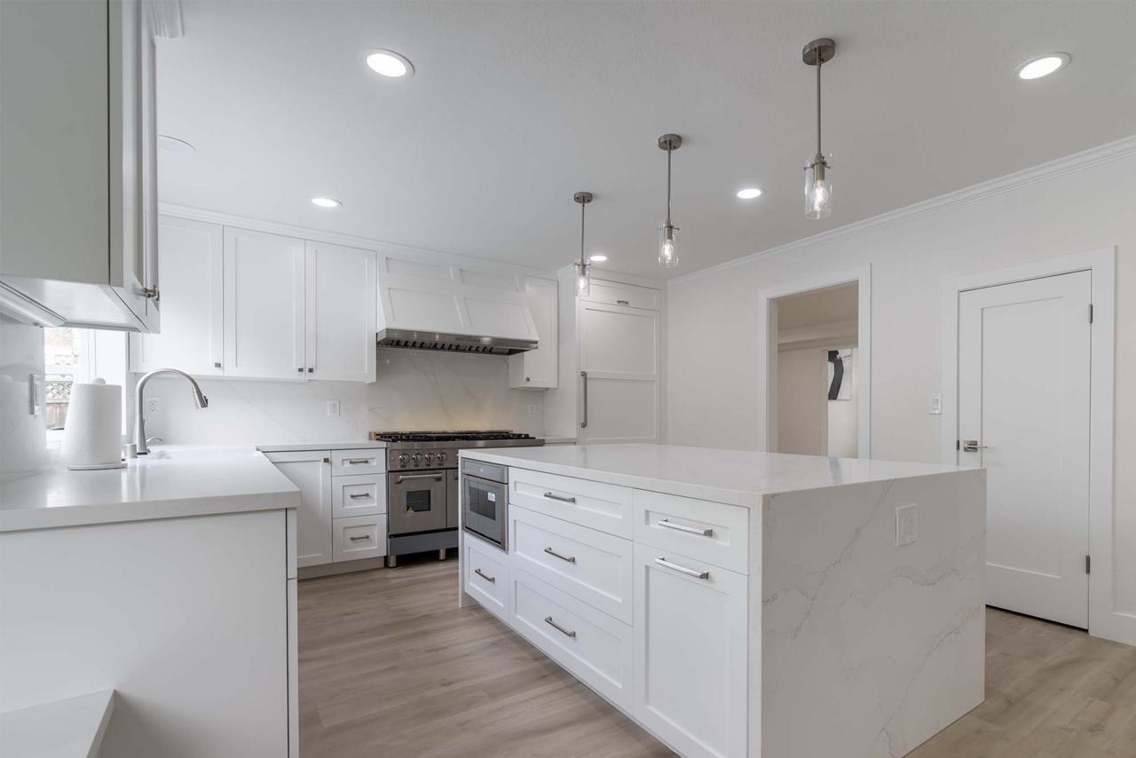 Kitchen featuring quartzite island with integrated microwave drawer, full slab backsplash, and designer pendant lighting