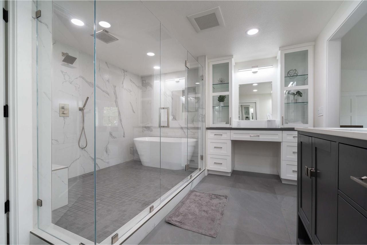 Primary wet room with frameless glass enclosure, freestanding tub, dual rain heads, and custom built-ins