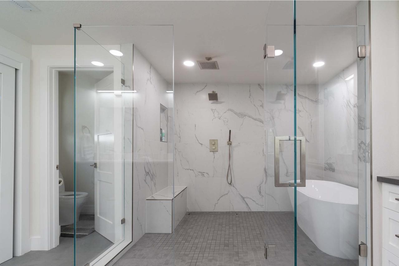 Primary wet room featuring freestanding tub, frameless glass enclosure, dual rain heads, and built-in bench seating