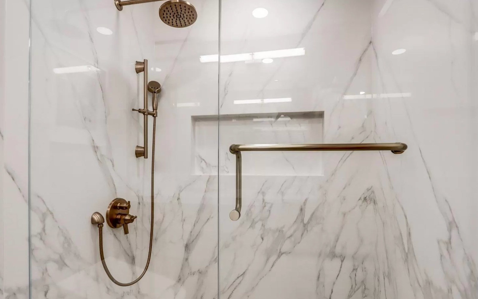 Bathroom featuring frameless walk-in glass shower, porcelain slabs, shampoo niche, and modern fixtures
