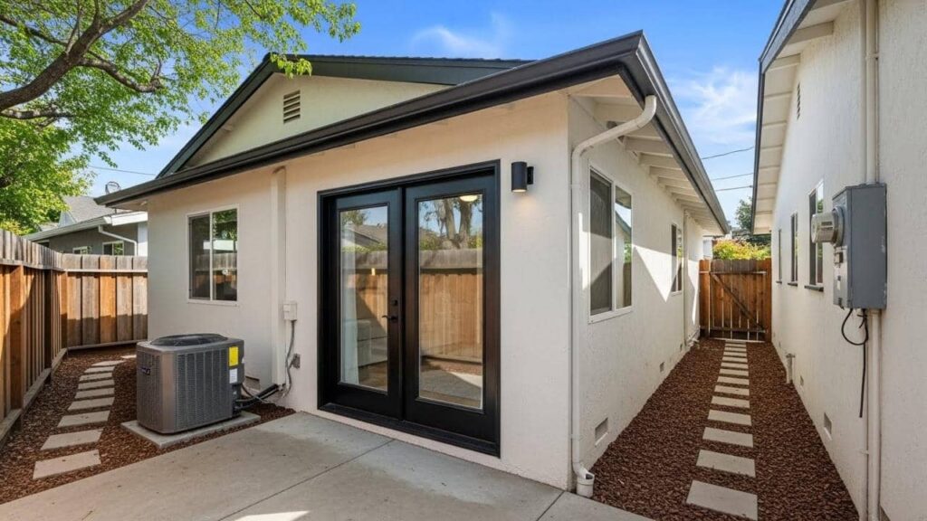 Finished stucco room addition with black-framed glass doors and a stepping-paver side yard path.