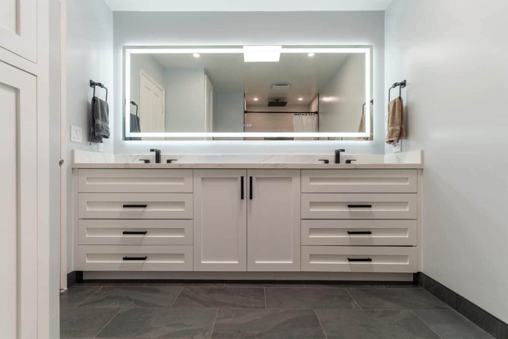 White double vanity with black hardware and a backlit mirror in a remodeled bathroom.