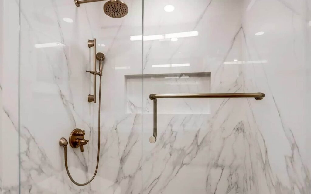 Marble-walled walk-in shower with brushed brass slide bar, rainfall showerhead, and grab bar.