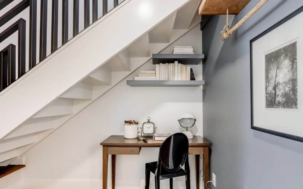 A cozy work nook built into the space beneath a staircase, complete with floating shelves and a small wood desk.