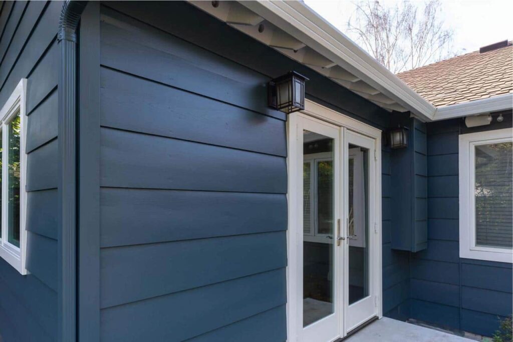 Close-up exterior corner of a room addition showing navy siding, white trim, and glass french doors.