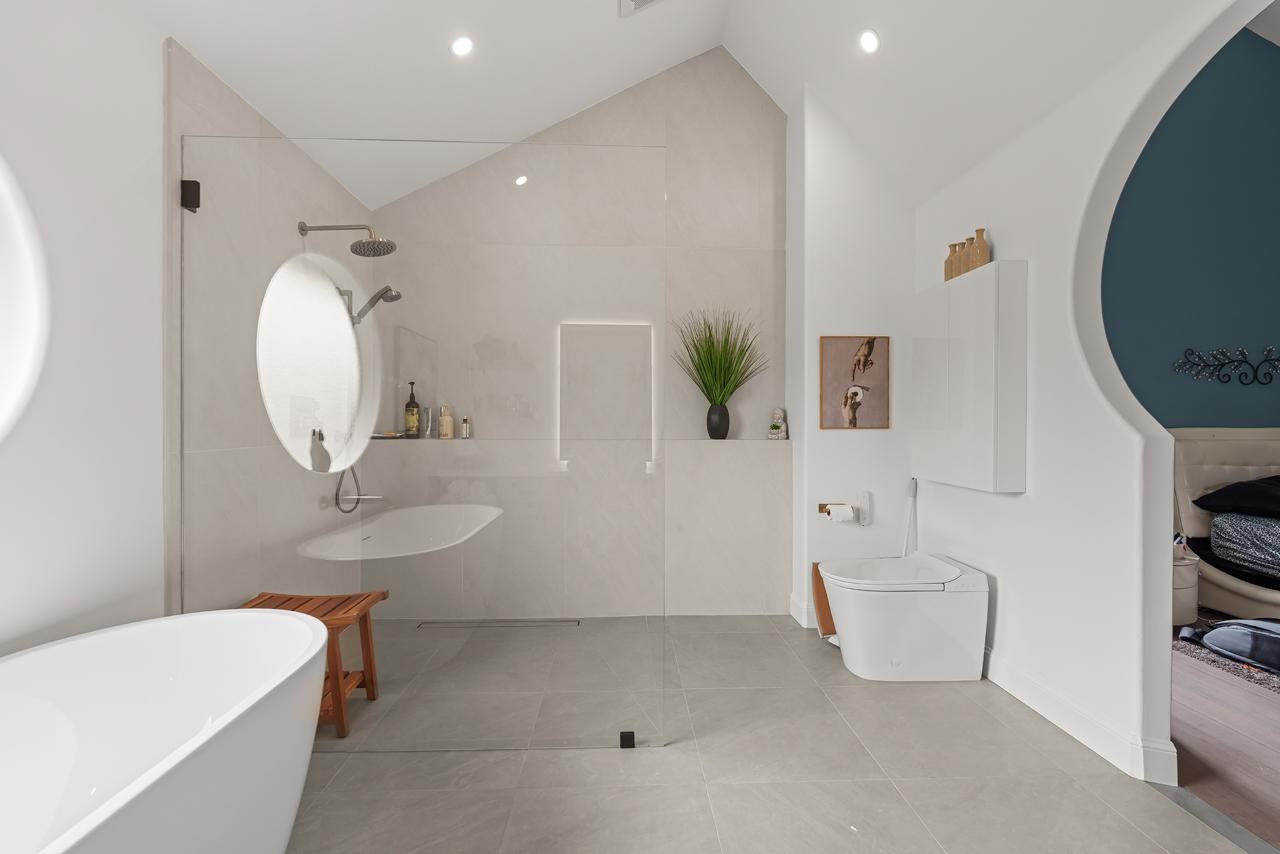 Primary bathroom after: open walk in shower with rain head with large format porcelain tile and white acrylic freestanding tub, by ASL Remodeling.