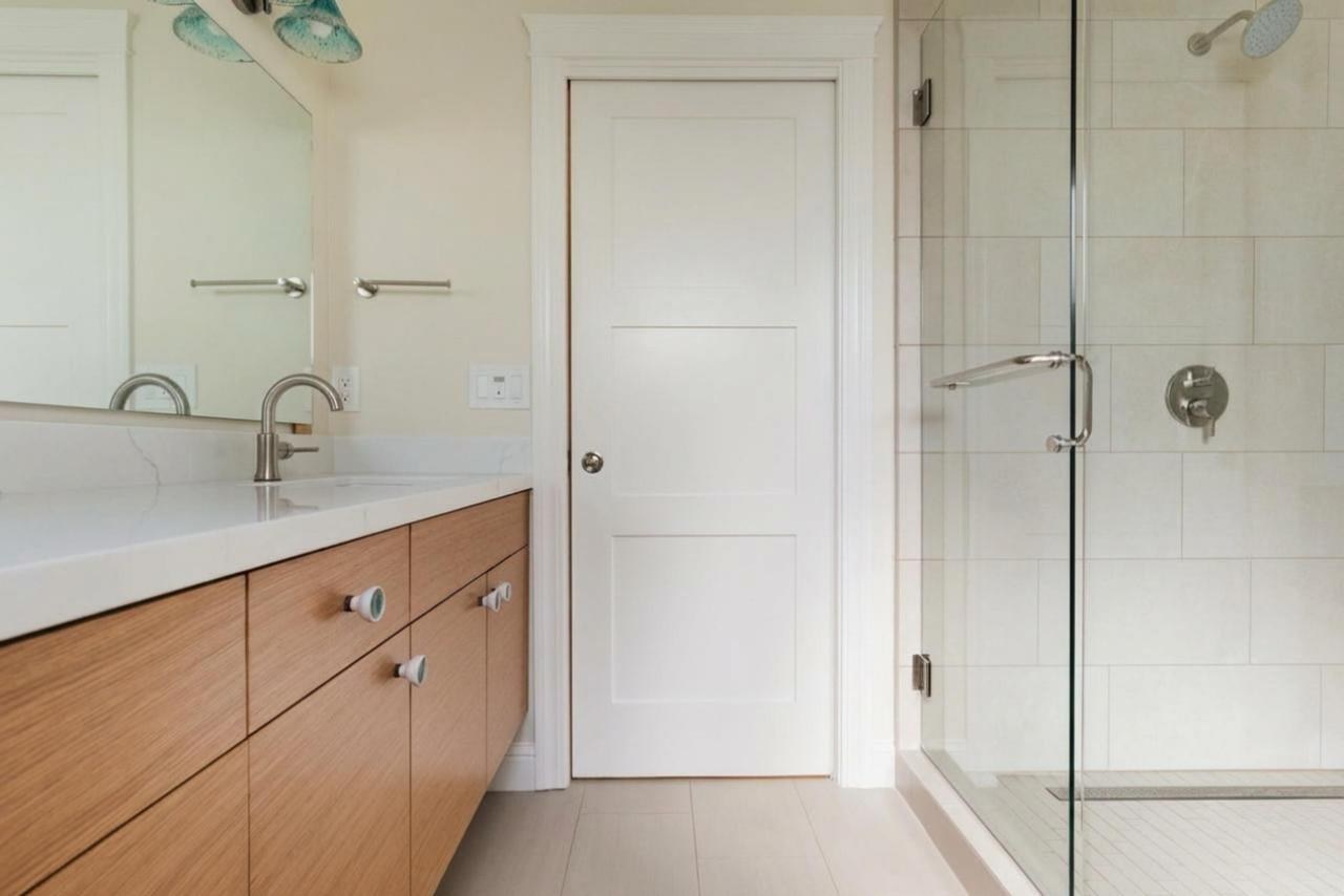 Primary bathroom after: wood vanity with glass enclosed shower with white quartz countertop and wood grain cabinetry, by ASL Remodeling.