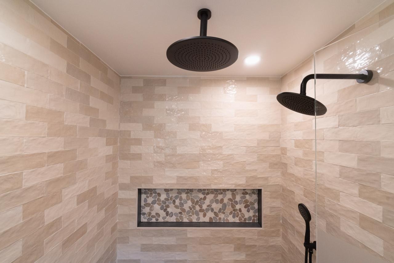 Primary bathroom: dual rain head shower with pebble niche with cream stacked tile and pebble mosaic tile, by ASL Remodeling.