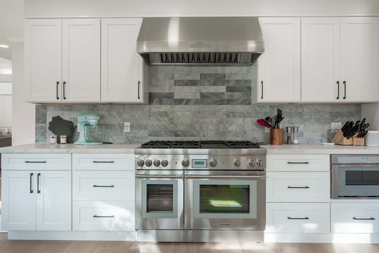 Kitchen with professional-grade range, tile backsplash, custom white cabinetry, and engineered white oak flooring
