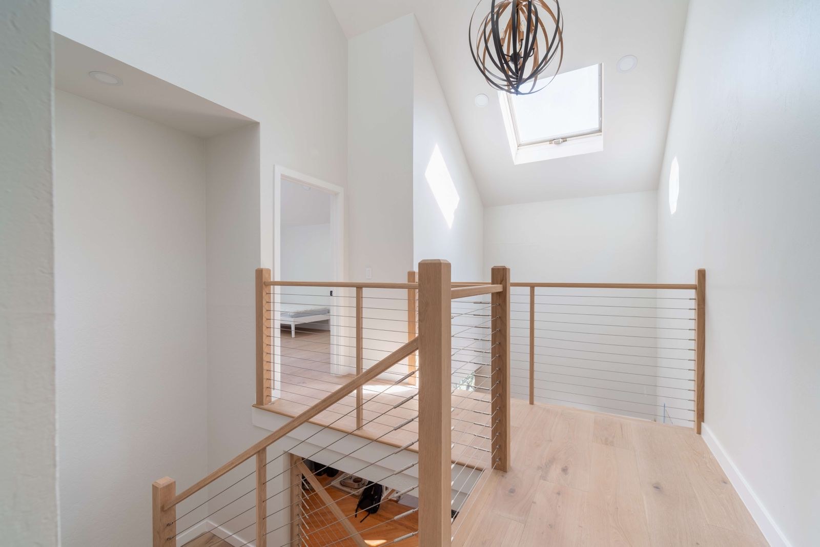 Upstairs landing with modern cable railing, skylight, engineered white oak hardwood flooring, and bright natural light